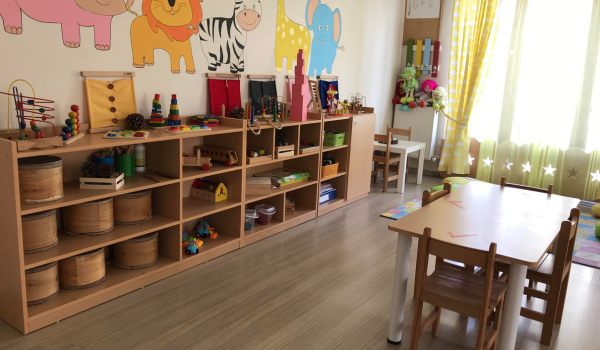 A bright daycare classroom with toy shelves and child-sized tables, featuring animal wall artwork