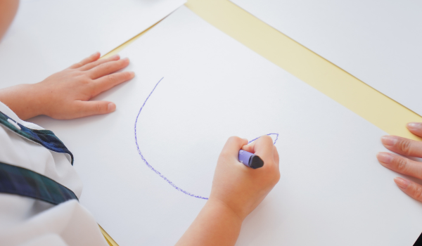 Close-up of a child drawing on white paper with a crayon