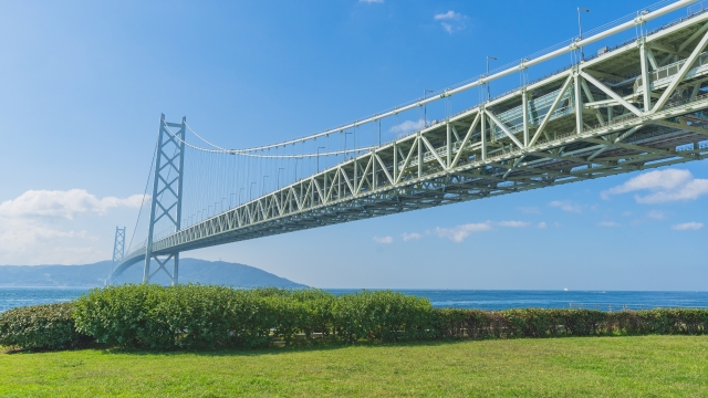 Akashi Kaikyo Bridge stretching over the sea under a clear blue sky, with a grassy foreground