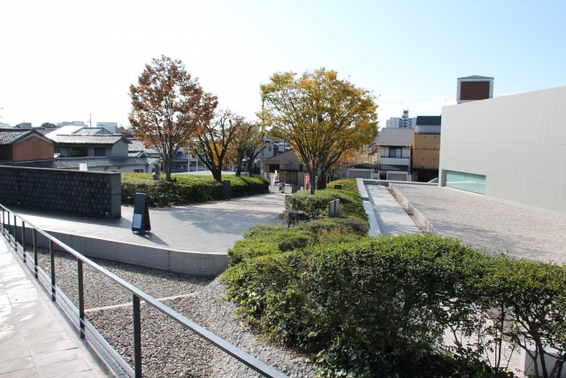 An outdoor plaza at the Himeji City Museum of Literature with greenery and a walkway, with town views beyond