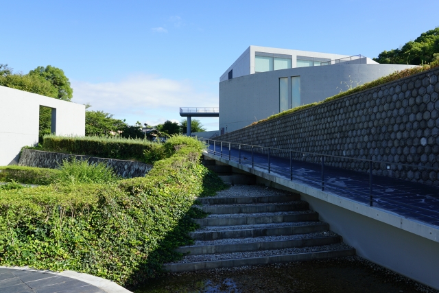 Exterior of the Himeji City Museum of Literature with a ramp and stairs along a stone wall, with greenery and blue sky