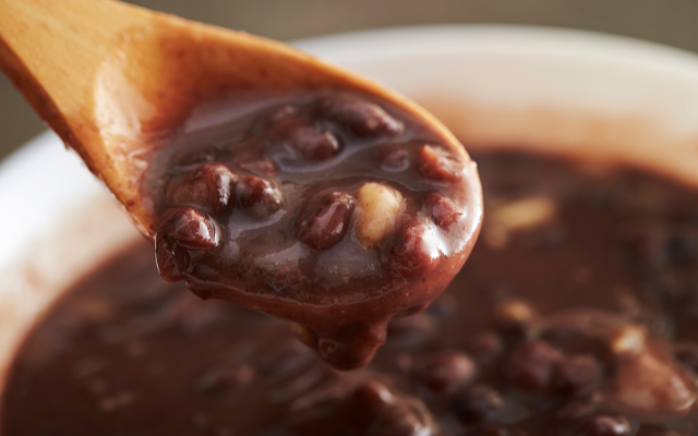 A close-up of a wooden spoon scooping sweet red bean soup