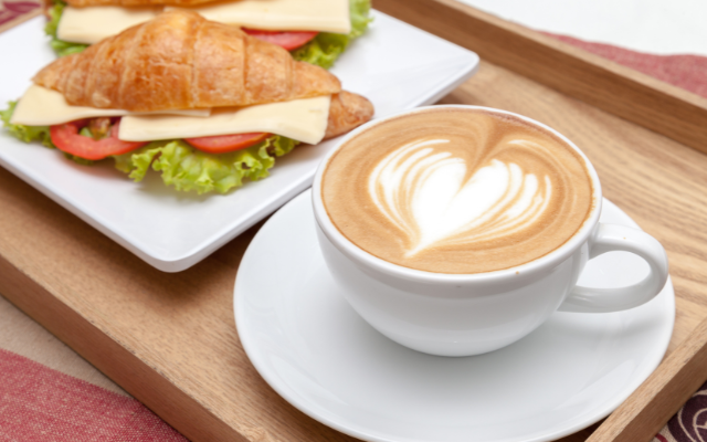 A latte with heart-shaped latte art and a croissant sandwich