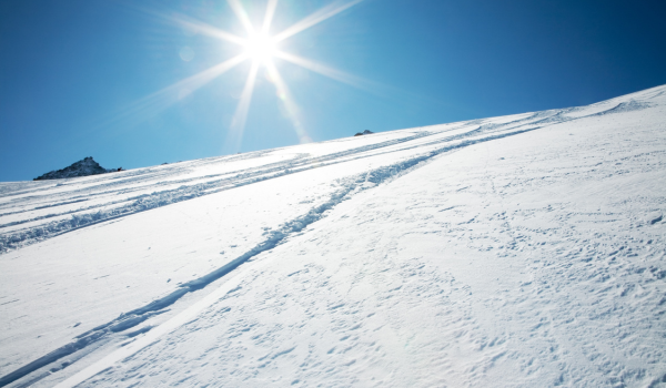 A snowy slope under a clear blue sky with bright sunshine