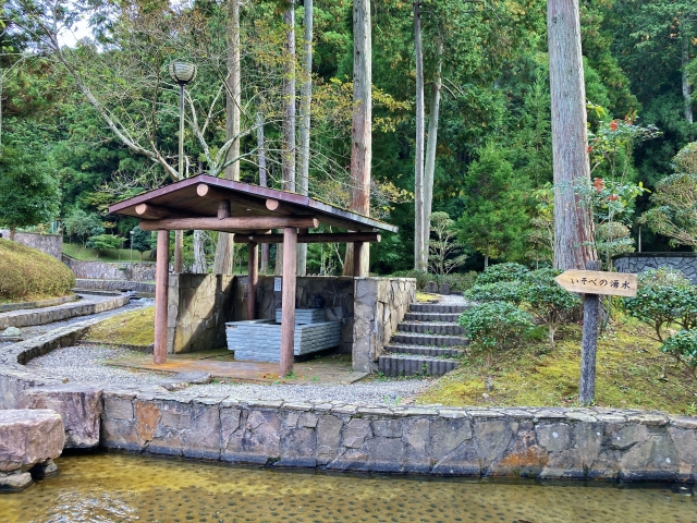 A gazebo and spring-water sign in a forested rest area at Mizuwakare Park