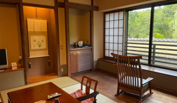 A traditional Japanese ryokan room with shoji screens, a low table, and a chair by the window