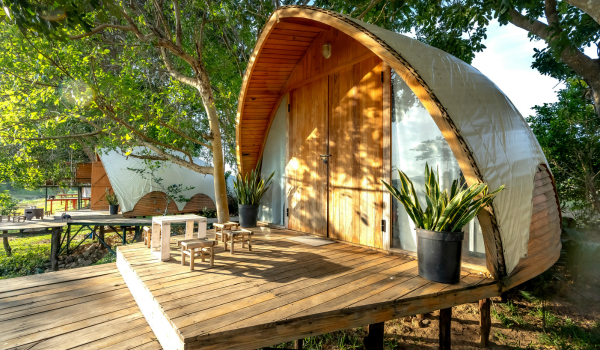 An arched glamping cabin in the woods with a wooden deck and outdoor seating