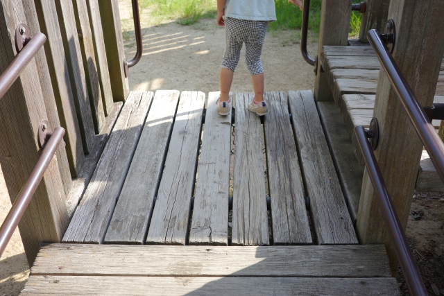 A child walking along a wooden play structure walkway with handrails